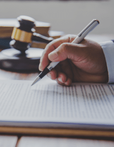 man's hand holding a pen over an employment contract with a legal gavel in the background